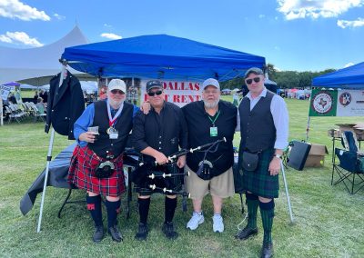 Group of four in kilts at the Dallas Kilt Rental tent at a Highland festival